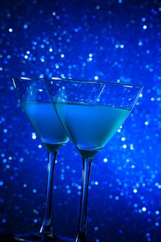 two glasses of blue cocktail on dark blue tint light bokeh background