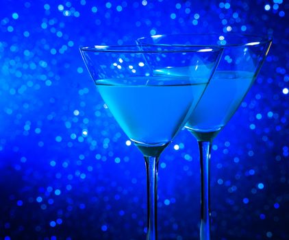 two glasses of blue cocktail on dark blue tint light bokeh background with space for text