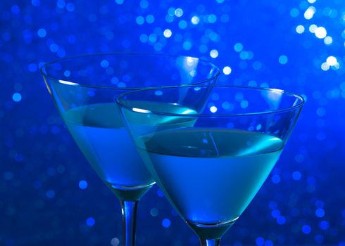 detail of a pair of glasses of blue cocktail on blue tint light bokeh background