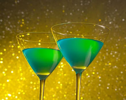 a pair of two glasses of green cocktail on golden tint light bokeh background