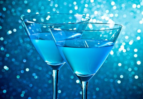 detail of a pair of glasses of blue cocktail on light blue tint bokeh background