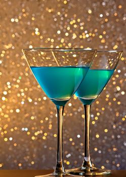 a pair of glasses of blue cocktail on golden tint light bokeh background on bar table