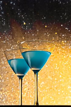 a pair of glasses of blue cocktail on golden tint light bokeh background
