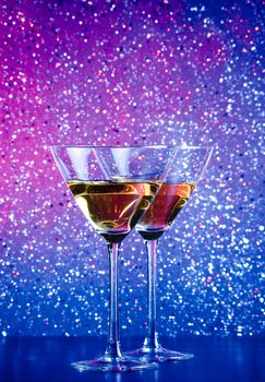a pair of glasses of cocktail on blue and violet tint light bokeh background on bar table