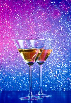 a pair of glasses of cocktail on blue and violet tint light bokeh background on bar table
