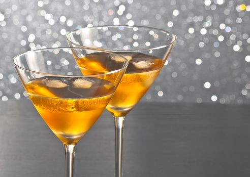 a pair of glasses of fresh cocktail with ice on silver tint light bokeh background with space for text