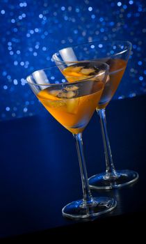 two glasses of  fresh cocktail with ice on blue tint light background on bar table