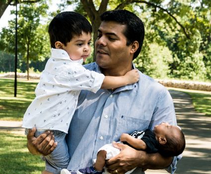 Latino father with his two young sons standing outside in a park with trees in the background