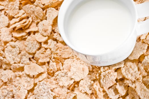 detail of cup of milk on corn flakes background, breakfast concept