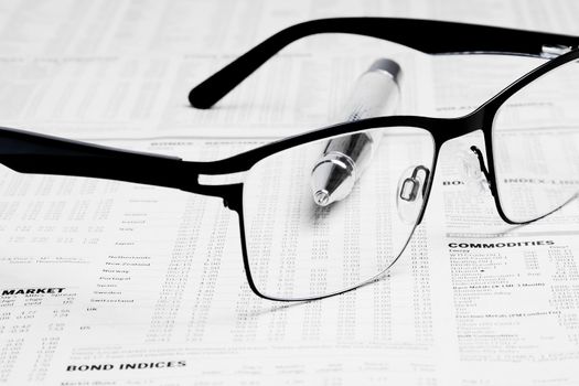 glasses over financial newspaper near near a business pen