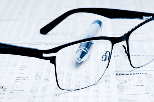 glasses over financial newspaper near near a business pen under light tint blue 