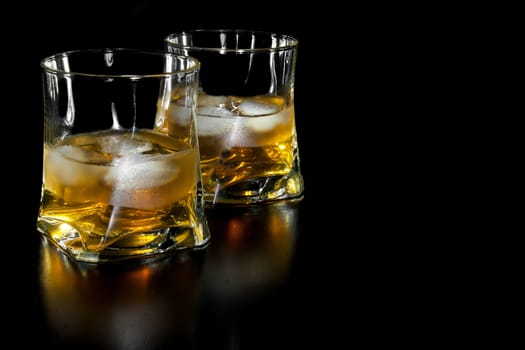 two glasses of whiskey with ice with space for text on black background