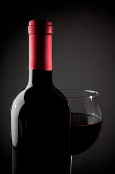 red wine glass near bottle on grey background