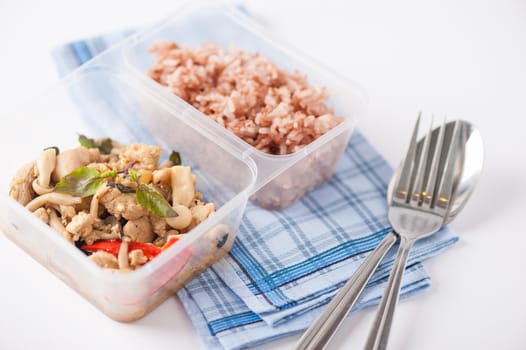 Stir freid basil with chicken breast and Termitomyces cooked by clean food concept with brown rice in lunch box on white table
