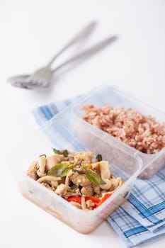 Stir freid basil with chicken breast and Termitomyces cooked by clean food concept with brown rice in lunch box on white table