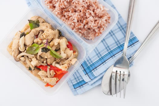 Stir freid basil with chicken breast and Termitomyces cooked by clean food concept with brown rice in lunch box on white table