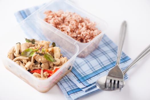 Stir freid basil with chicken breast and Termitomyces cooked by clean food concept with brown rice in lunch box on white table