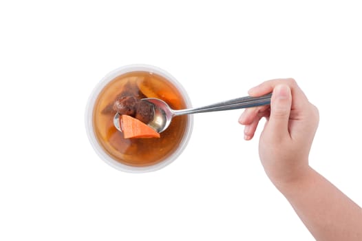 Vegetables soup cooked by clean food concept in lunch box on white table with female right hand holding spoon with soup and carrot isolated on white background
