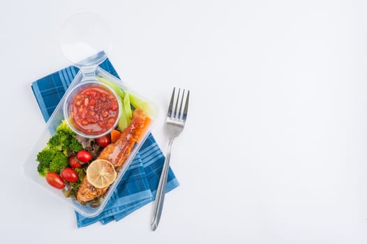 Grilled salmon with tomato salsa and salad cooked by clean food concept in lunch box on white table