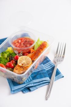 Grilled salmon with tomato salsa and salad cooked by clean food concept in lunch box on white table