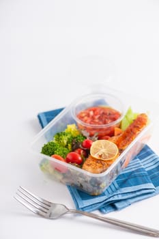 Grilled salmon with tomato salsa and salad cooked by clean food concept in lunch box on white table