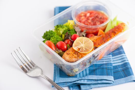 Grilled salmon with tomato salsa and salad cooked by clean food concept in lunch box on white table