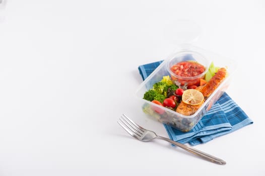 Grilled salmon with tomato salsa and salad cooked by clean food concept in lunch box on white table