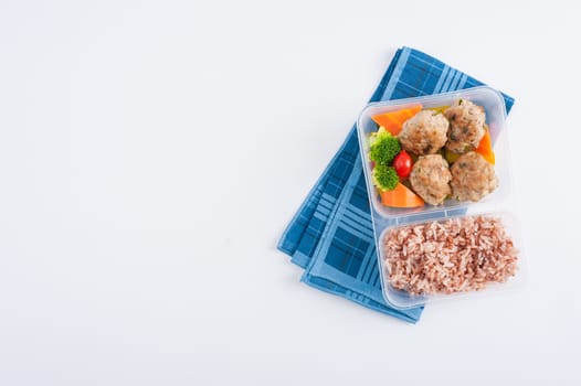 Thai style fried pork ball cooked by clean food concept with vegetables and brown rice in lunch box on white table