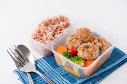 Thai style fried pork ball cooked by clean food concept with vegetables and brown rice in lunch box on white table