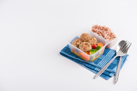Thai style fried pork ball cooked by clean food concept with vegetables and brown rice in lunch box on white table