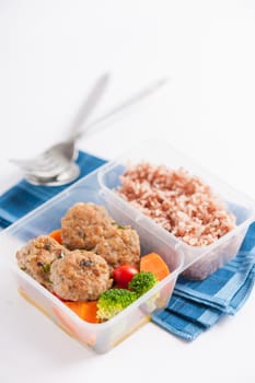 Thai style fried pork ball cooked by clean food concept with vegetables and brown rice in lunch box on white table