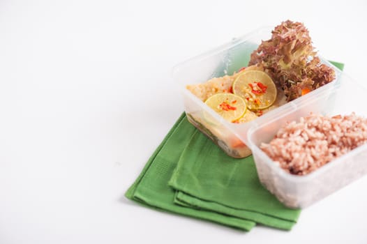 Thai style steamed fish in spicy lemon sauce cooked by clean food concept with vegetables and brown rice in lunch box on white table