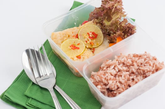 Thai style steamed fish in spicy lemon sauce cooked by clean food concept with vegetables and brown rice in lunch box on white table