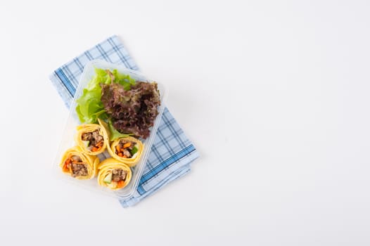 Thai spicy egg rolls (Fresh spring rolls, Kuay Teaw Lui Suan but use egg replace to rice sheet) with tofu, minced pork and vegetables cooked by clean food concept in lunch box on white table