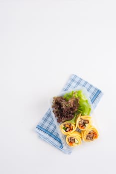 Thai spicy egg rolls (Fresh spring rolls, Kuay Teaw Lui Suan but use egg replace to rice sheet) with tofu, minced pork and vegetables cooked by clean food concept in lunch box on white table