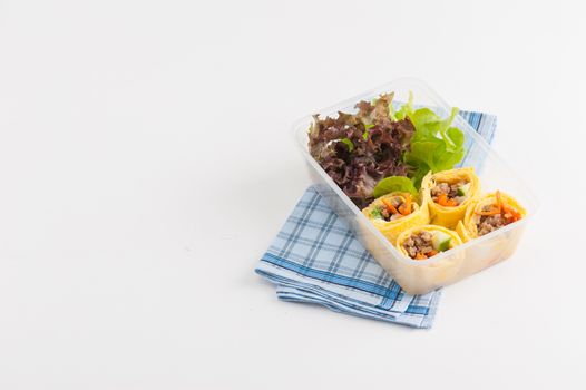Thai spicy egg rolls (Fresh spring rolls, Kuay Teaw Lui Suan but use egg replace to rice sheet) with tofu, minced pork and vegetables cooked by clean food concept in lunch box on white table