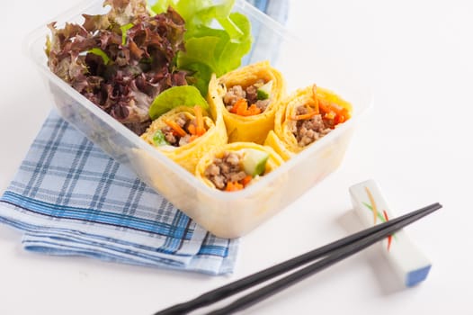 Thai spicy egg rolls (Fresh spring rolls, Kuay Teaw Lui Suan but use egg replace to rice sheet) with tofu, minced pork and vegetables cooked by clean food concept in lunch box on white table