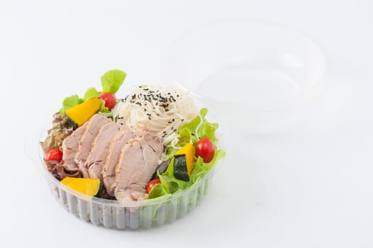 Salad with roasted pork and soba noodles by clean food concept in lunch box on white table