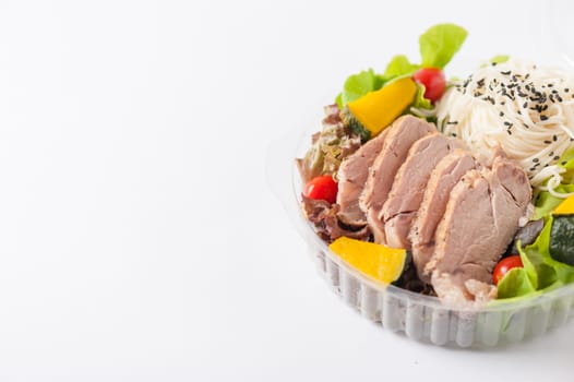 Salad with roasted pork and soba noodles by clean food concept in lunch box on white table