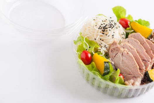 Salad with roasted pork and soba noodles by clean food concept in lunch box on white table
