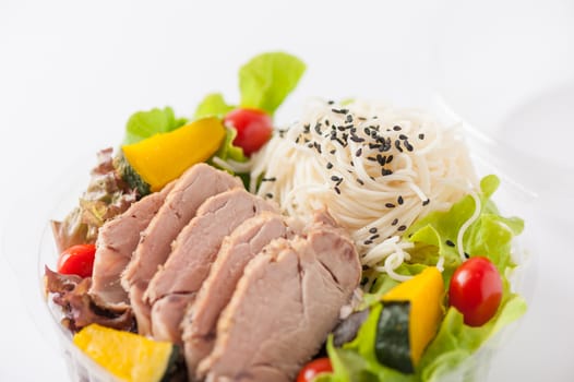 Salad with roasted pork and soba noodles by clean food concept in lunch box on white table