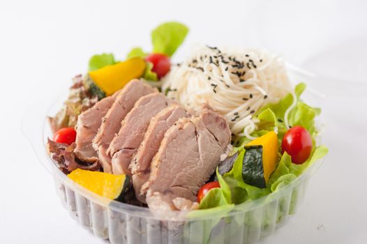 Salad with roasted pork and soba noodles by clean food concept in lunch box on white table