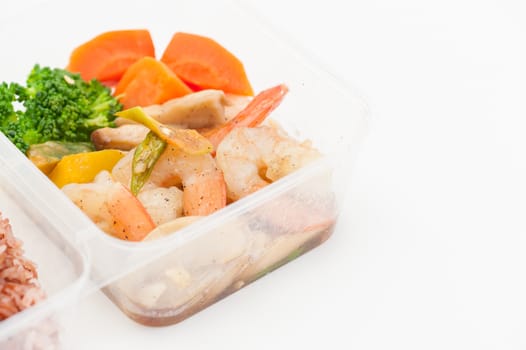 Thai style spicy stir fried shrimps cooked by clean food concept with brown rice and vegetables in lunch box on white table
