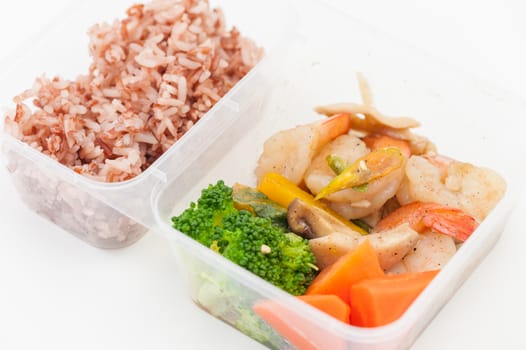 Thai style spicy stir fried shrimps cooked by clean food concept with brown rice and vegetables in lunch box on white table