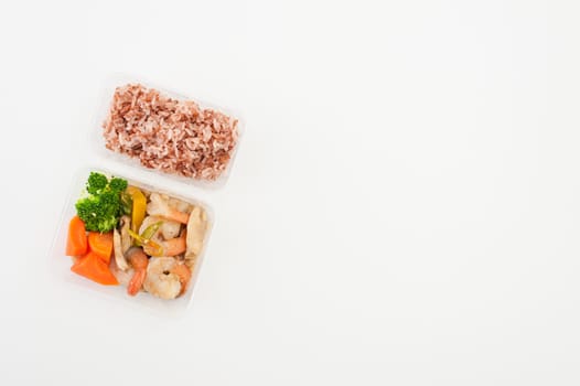 Thai style spicy stir fried shrimps cooked by clean food concept with brown rice and vegetables in lunch box on white table