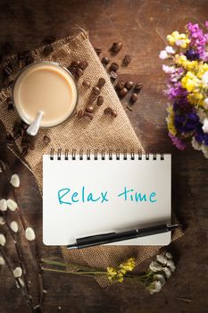 "Relax time" is written on Notepad with pen, a glass of Thai tea and bits of red velvet cake on rustic wood background with low key scene