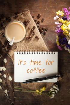 "It's time for coffee" is written on Notepad with pen, a glass of Thai tea and bits of red velvet cake on rustic wood background with low key scene