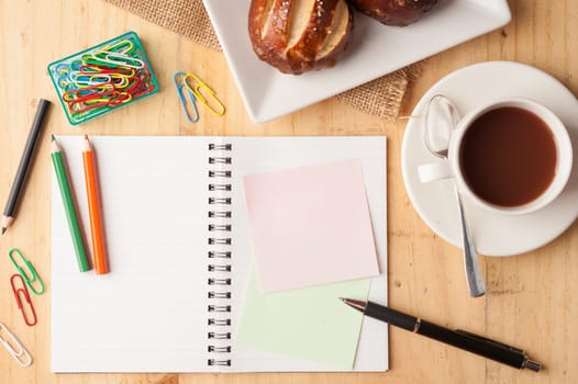 Notebook and sticky paper, paper clip, color pencil, and pen on wood table in vintage style