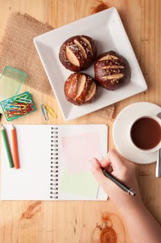 Notebook and sticky paper, paper clip, color pencil, and pen on wood table in vintage style with female right hand wrting on notepad