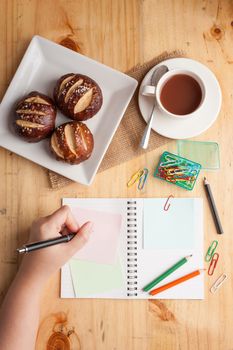 Notebook and sticky paper, paper clip, color pencil, and pen on wood table in vintage style with female hand wrting on notepad